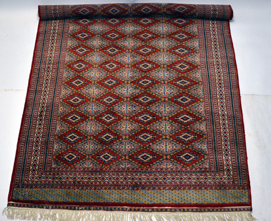 Lot 304: Hand woven red Pakistan wool carpet with lozenge geometrical pattern. 310 x 184cm.