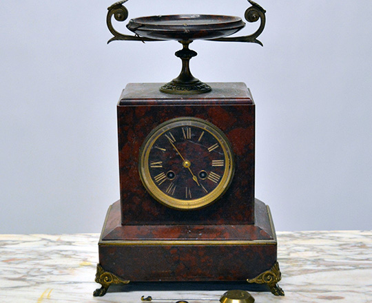 Lot 584: 19th c Nap.lll red marble mantle clock topped with a dish and a pair of cassolettes with repair on dishes.
